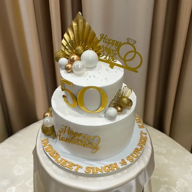 A Golden 50th Anniversary Cake — A two-tier gold and white cake marking fifty years together, finished with pearl accents and a hand-lettered gold message.