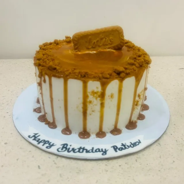 A Lotus Biscoff Drip Cake — A caramel drip cake finished with crushed Biscoff crumble and a whole Lotus biscuit, hand-lettered on the base.