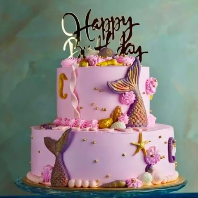 A Mermaid Birthday Cake — A two-tier pink birthday cake with hand-sculpted mermaid tails, gold starfish, and a hand-lettered topper.