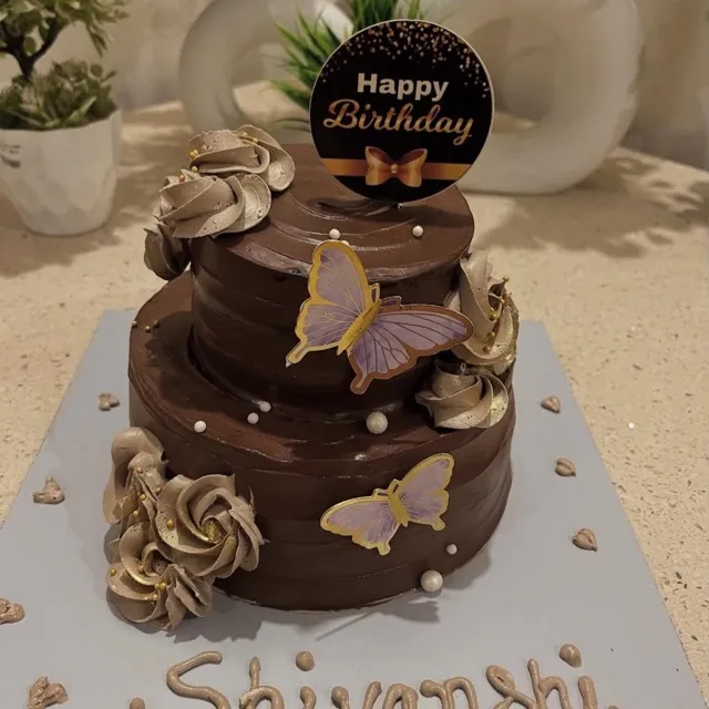 A Butterfly Birthday Cake for Shivanshi — A two-tier dark chocolate cake with bronze-gold buttercream rosettes, purple-and-gold butterfly toppers, and edible pearls, finished with a piped name plaque.