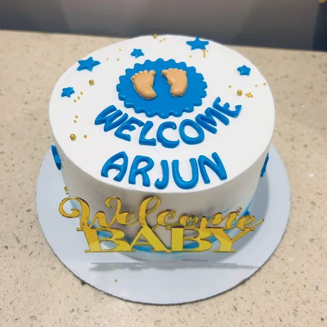 A Welcome Baby Cake for Arjun — Piped blue stars and tiny fondant footprints welcome the newest arrival, finished with a gold mirrored topper.